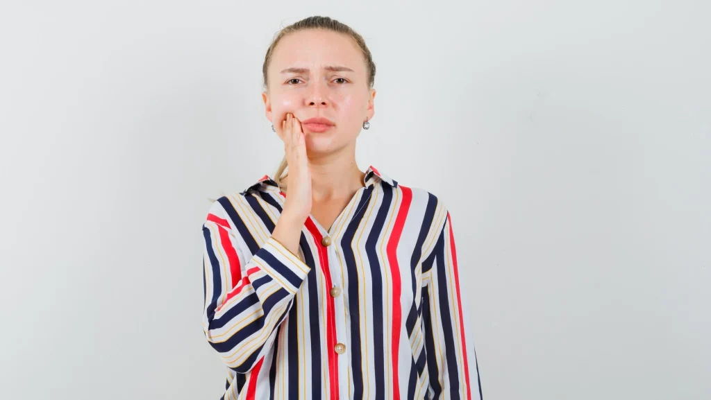 Mulher com expressão de desconforto segurando o rosto, representando as alterações bucais como mucosite, xerostomia e dor gengival comuns durante a quimioterapia e radioterapia